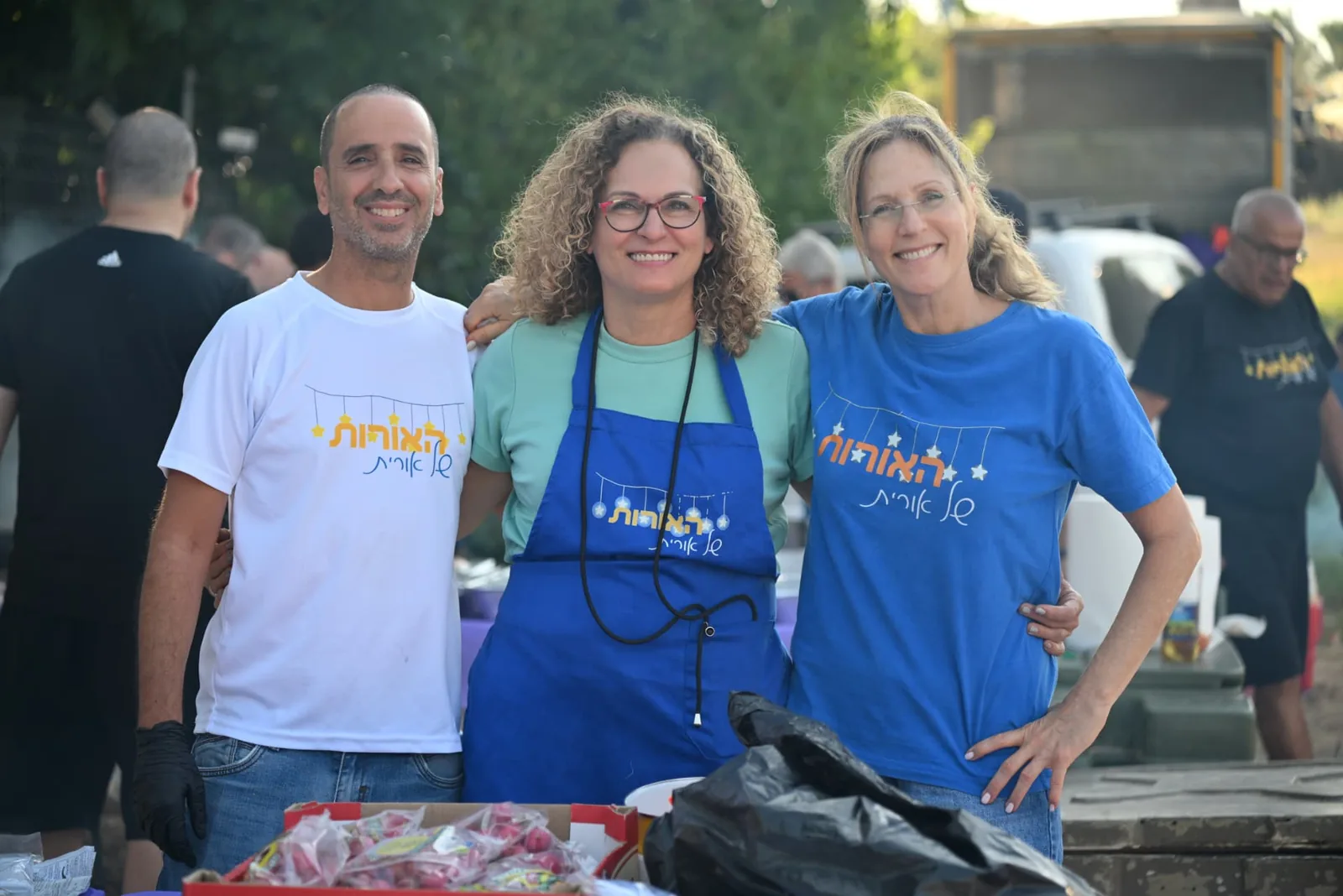 Three volunteers in Lights of Orit shirts and aprons