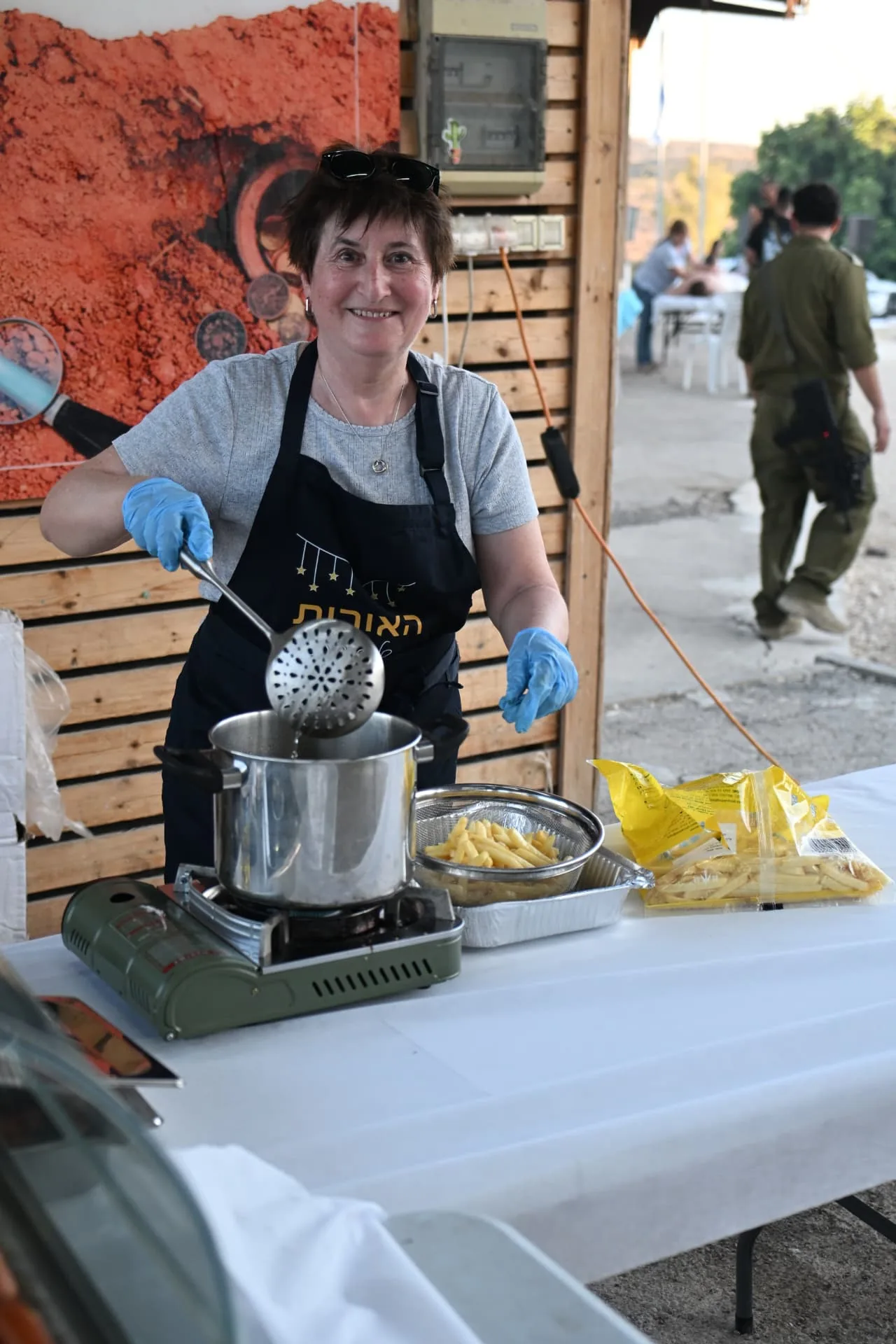 A smiling volunteer frying fresh chips at a field kitchen station