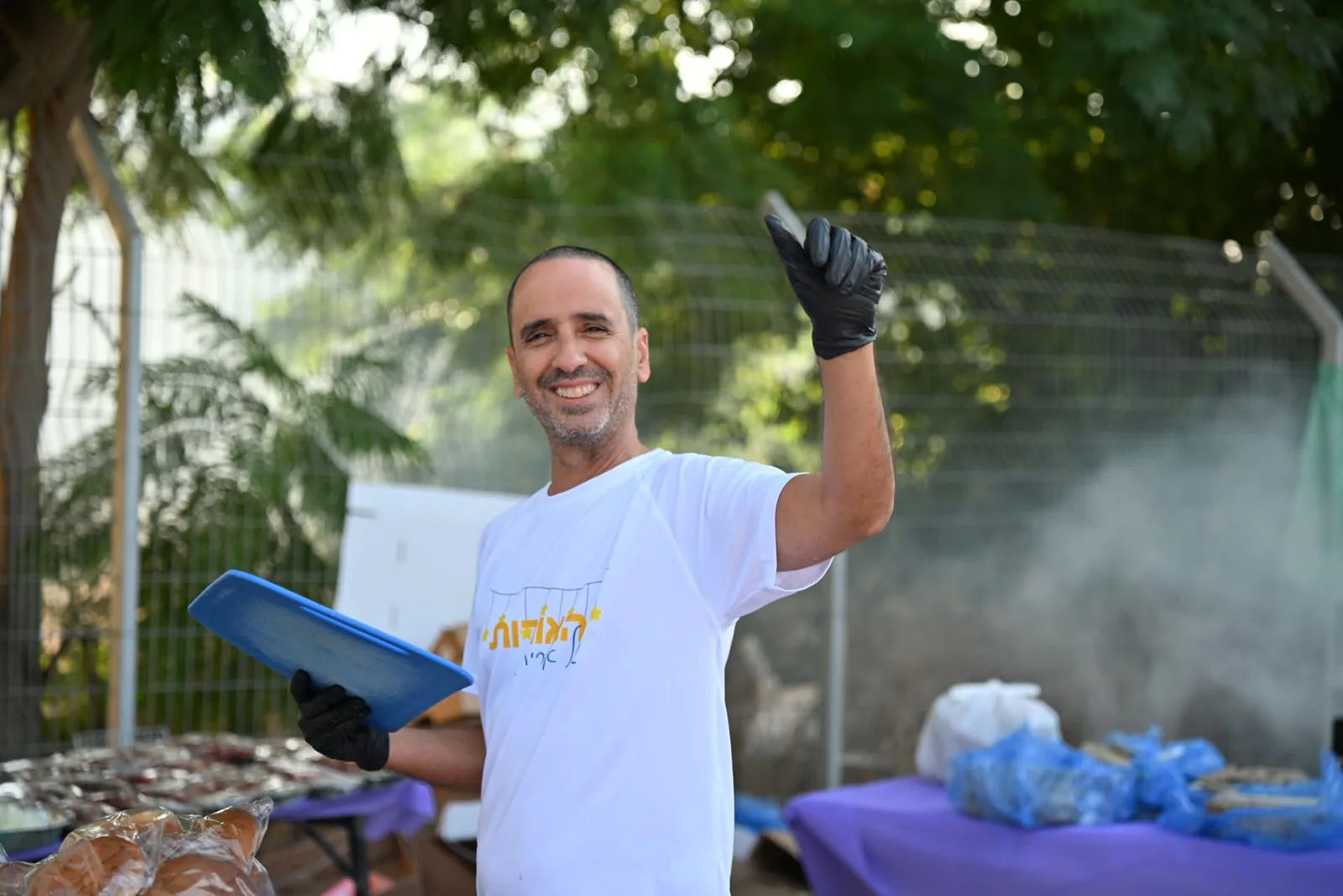 A volunteer in a Lights of Orit shirt cheers at the grill
