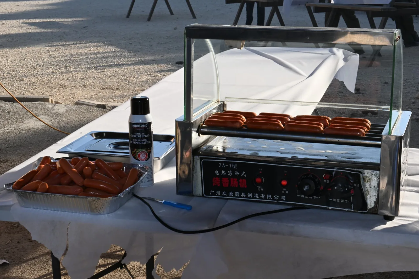 Hot dogs warming on a rolling grill at the serving table in the late afternoon light