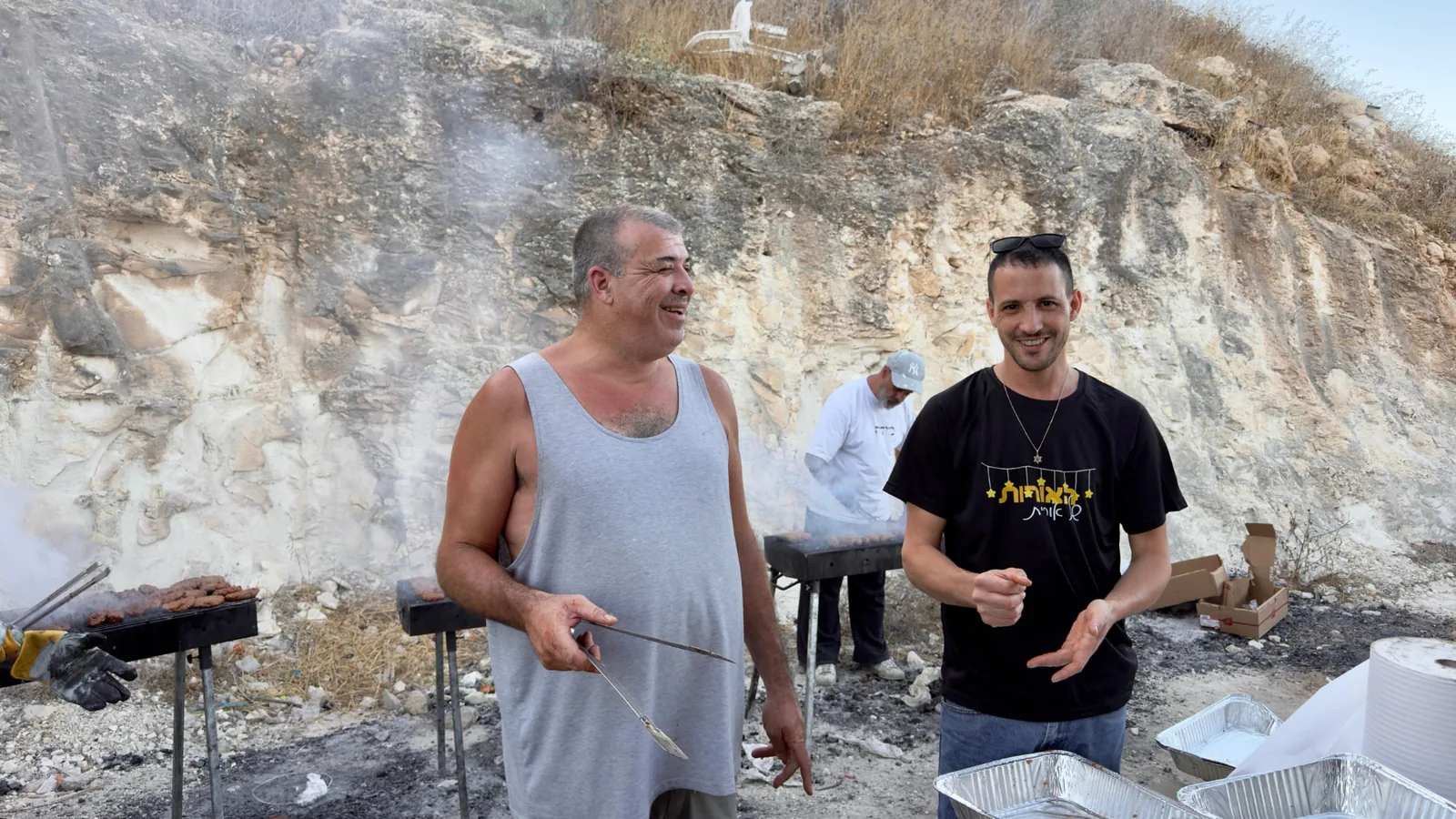 Volunteers grilling kebabs over open coals at the hillside barbecue