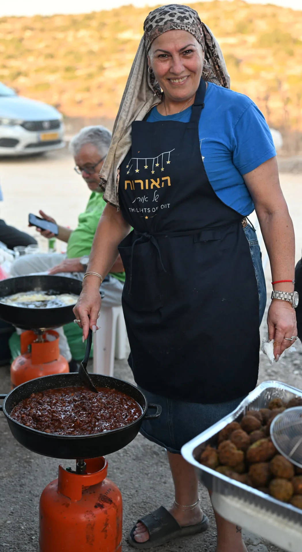 A volunteer cooking a pan of shakshuka over a field burner