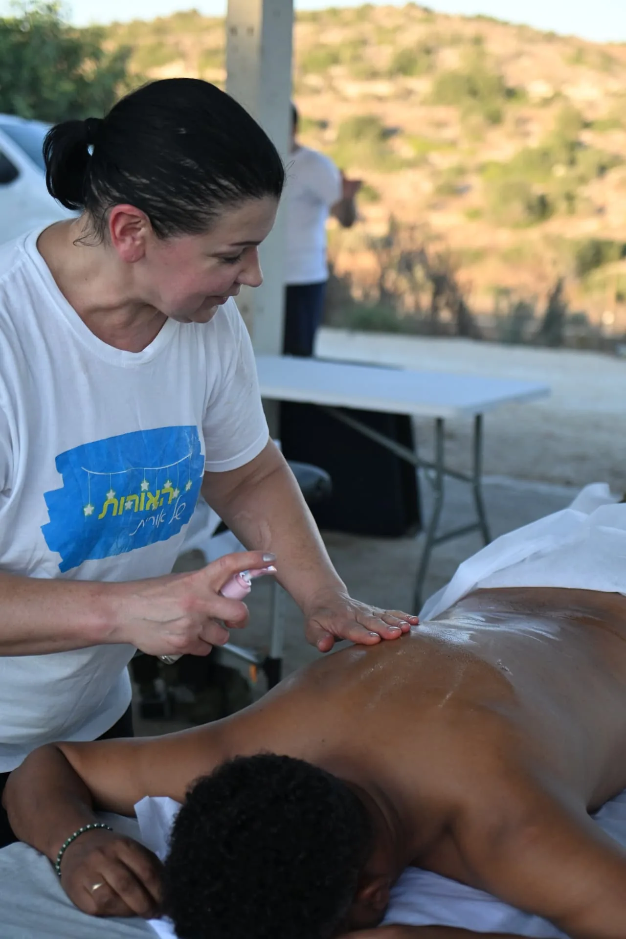 A volunteer in a Lights of Orit shirt applying massage oil for a soldier