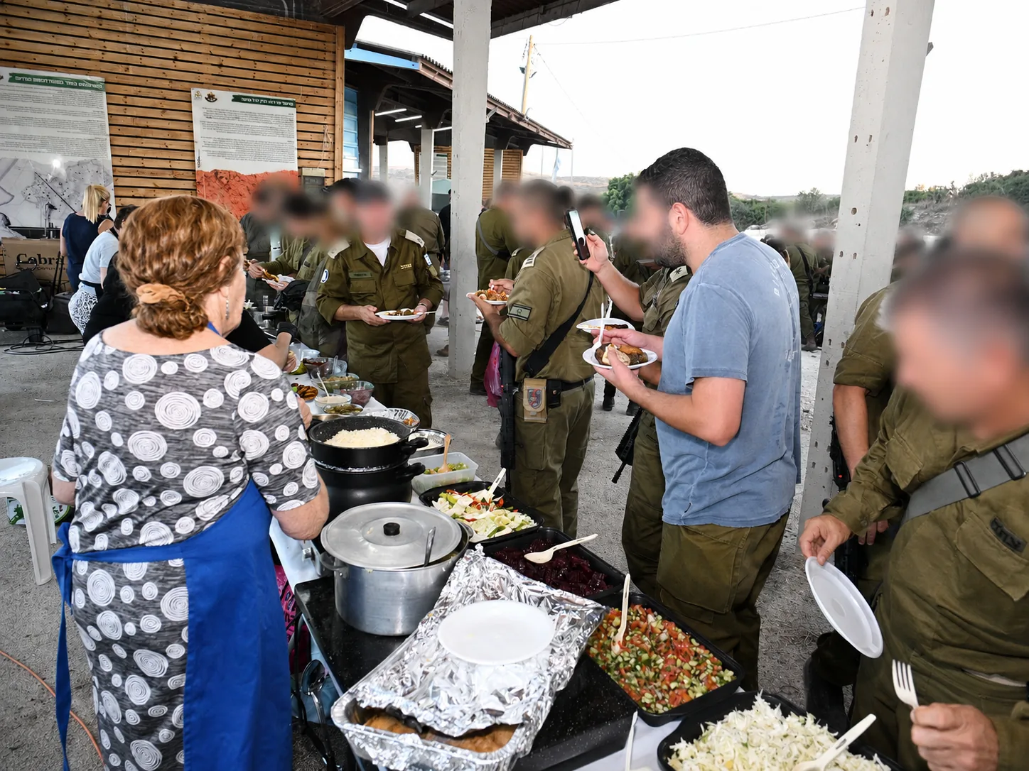 Volunteers serving home-cooked dishes to soldiers under a shaded shelter