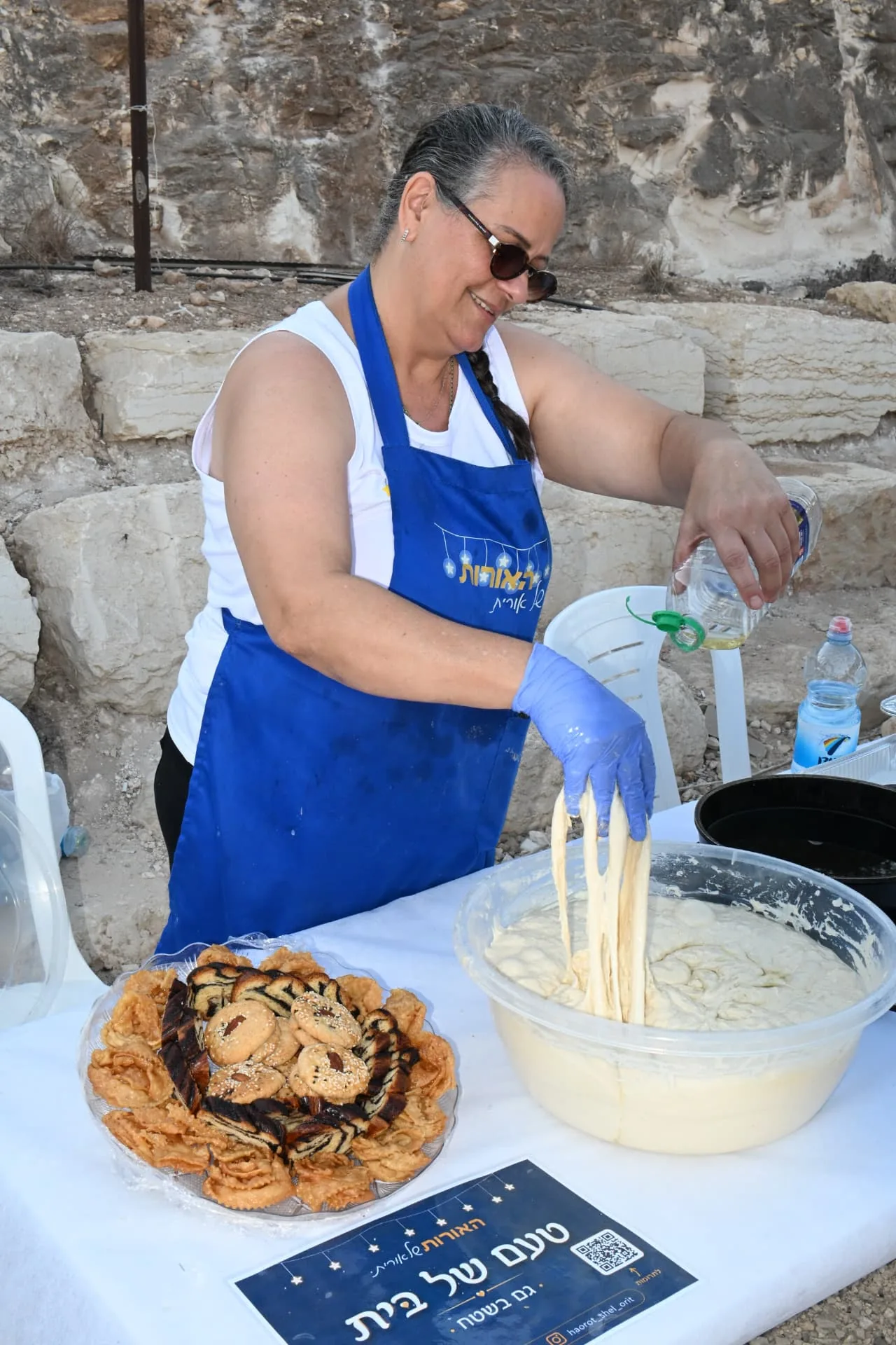 A volunteer in a Lights of Orit apron stretching fresh dough beside a tray of home-baked pastries