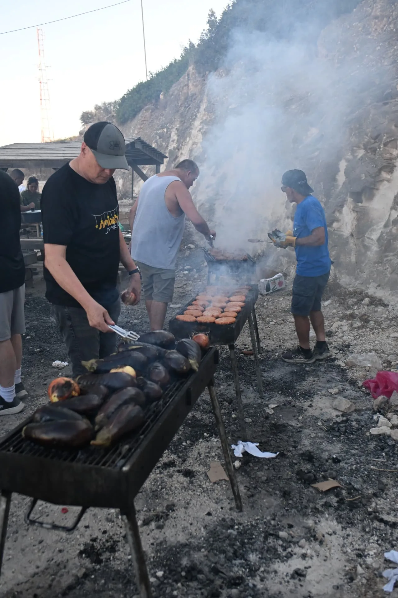 Volunteers grilling kebabs and aubergines over open coals at the hillside base