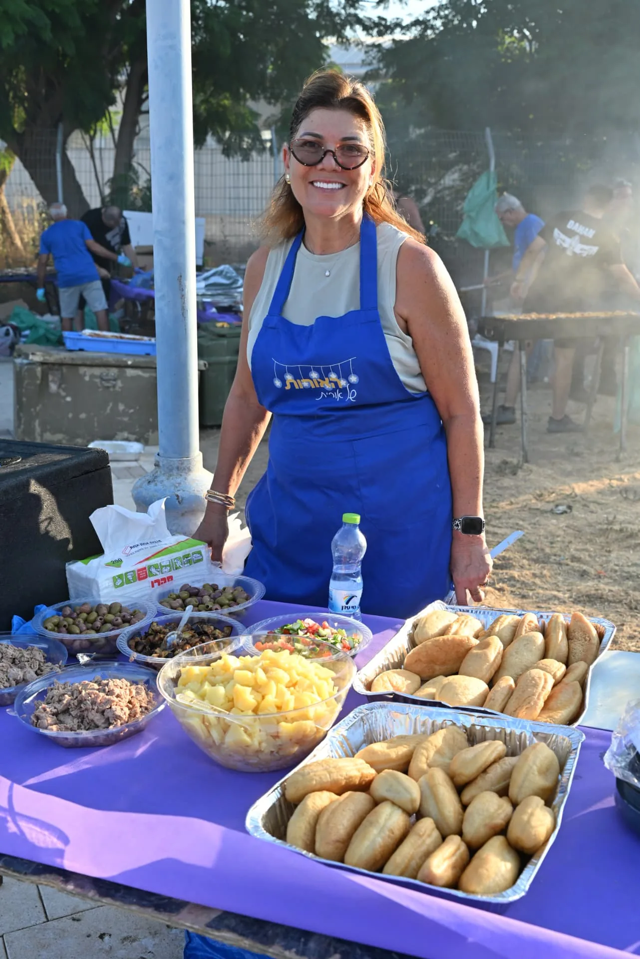 Volunteer in a Lights of Orit apron beside trays of fresh food