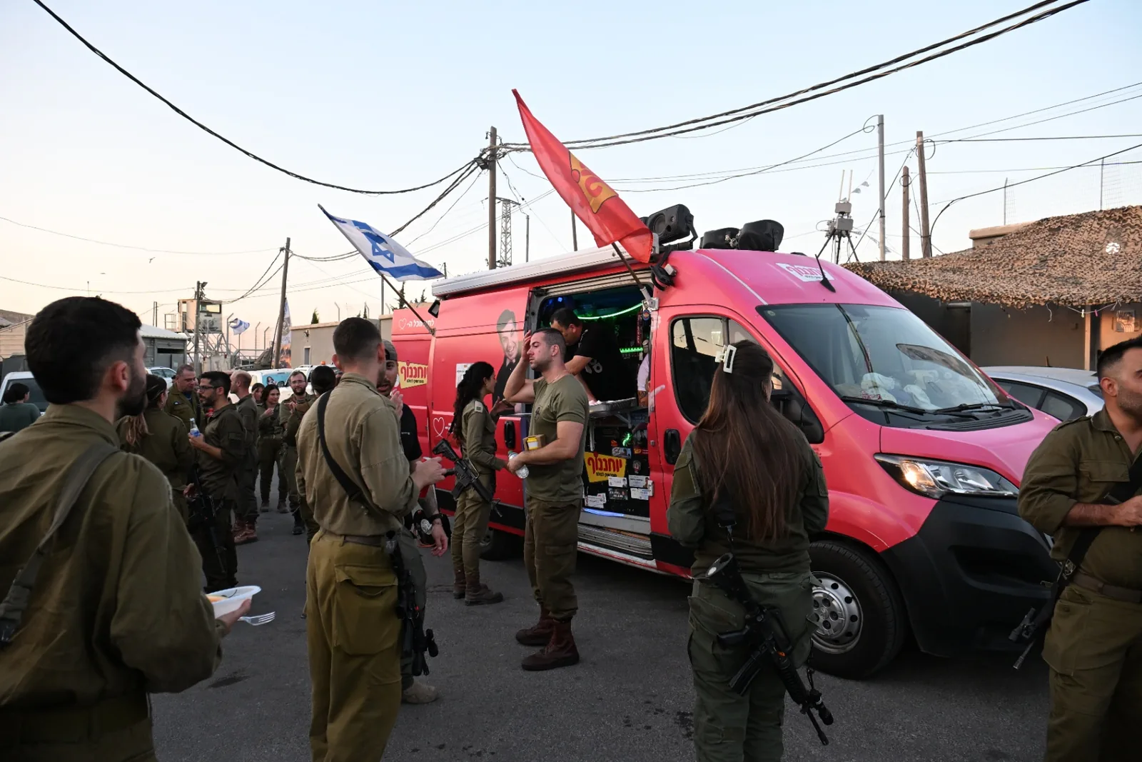 Soldiers gathering around a food truck under Israeli flags at dusk