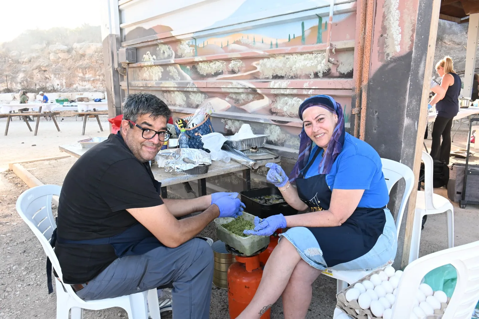 Two volunteers preparing fresh dishes together in the shade of the field kitchen