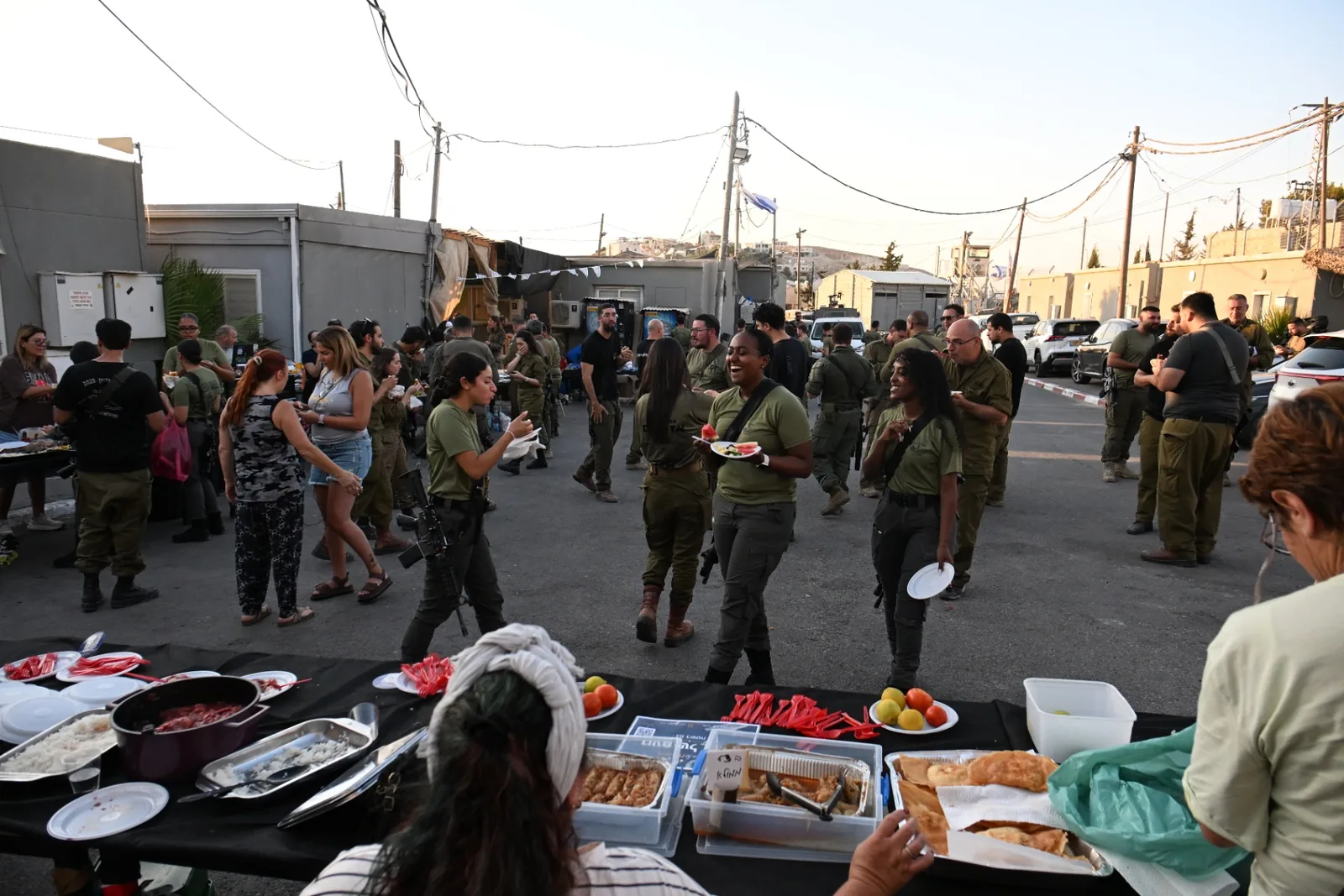 Soldiers and volunteers gathered around laden buffet tables at sunset