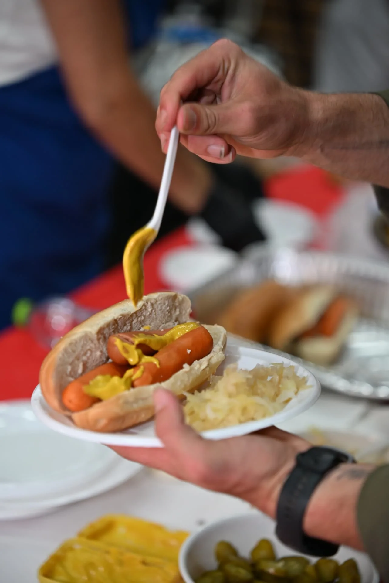 Mustard being added to a hot dog plate