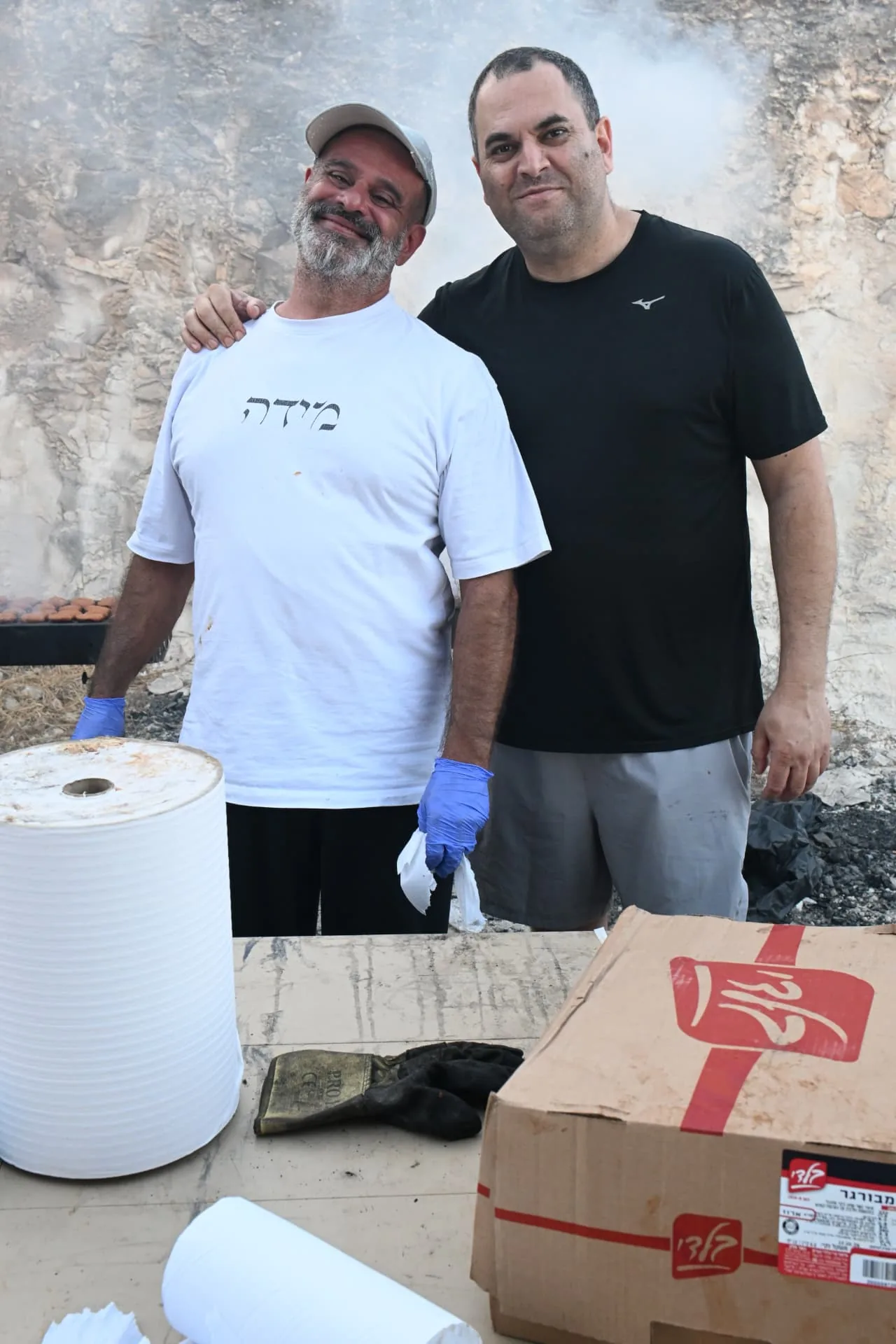 Two volunteers side by side at the grilling station, smiling between rounds of cooking