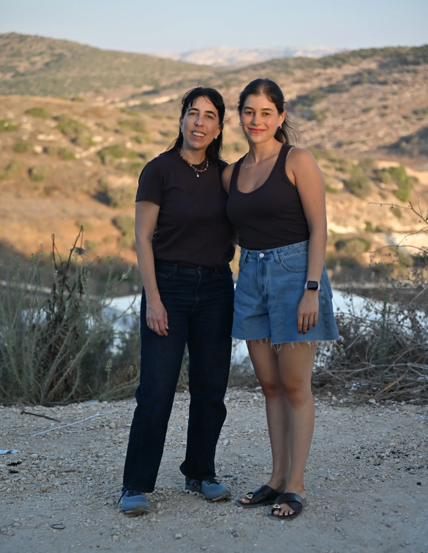 Two volunteers standing together in the hills at sunset