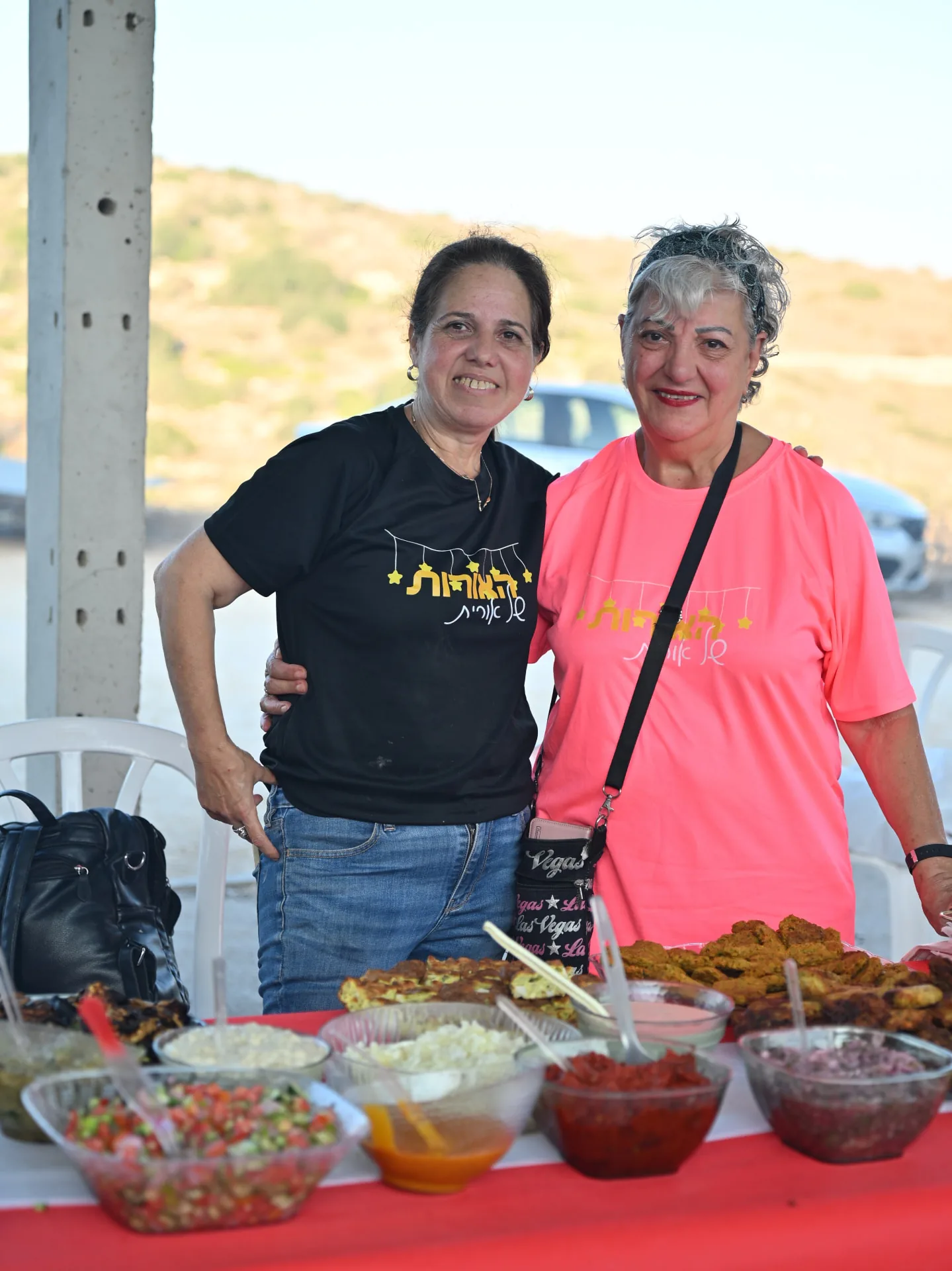 Two volunteers beside a spread of salads and pastries