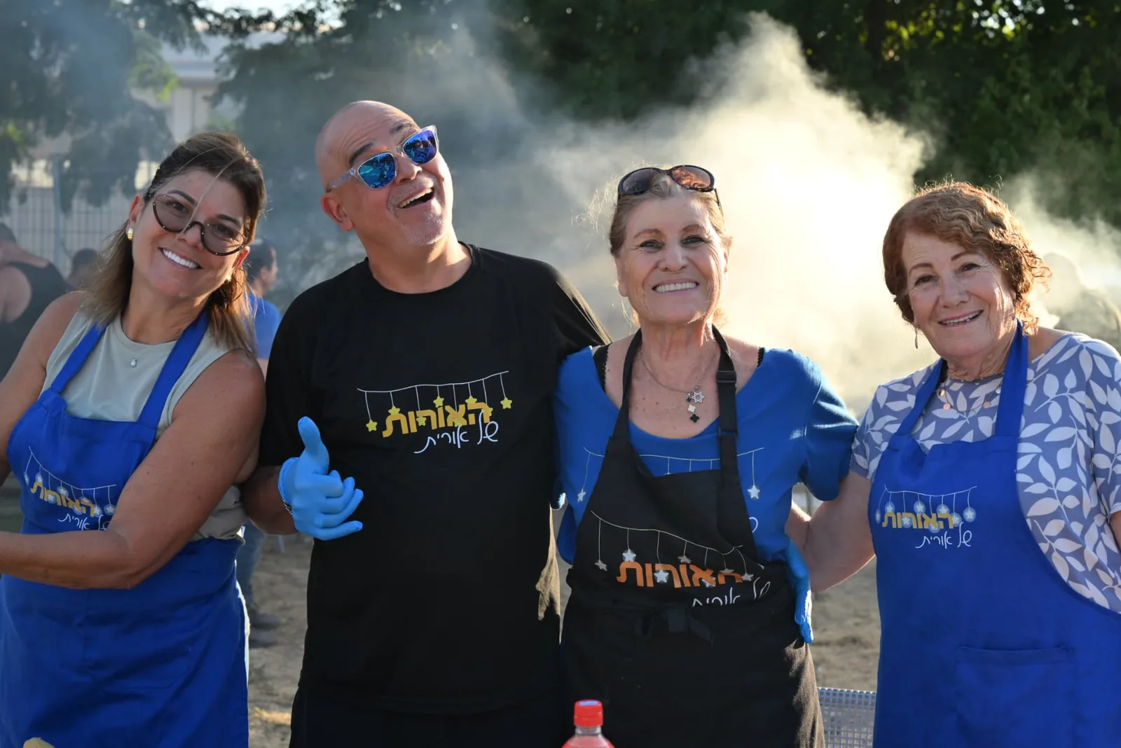 Smiling volunteers in Lights of Orit aprons by the grill