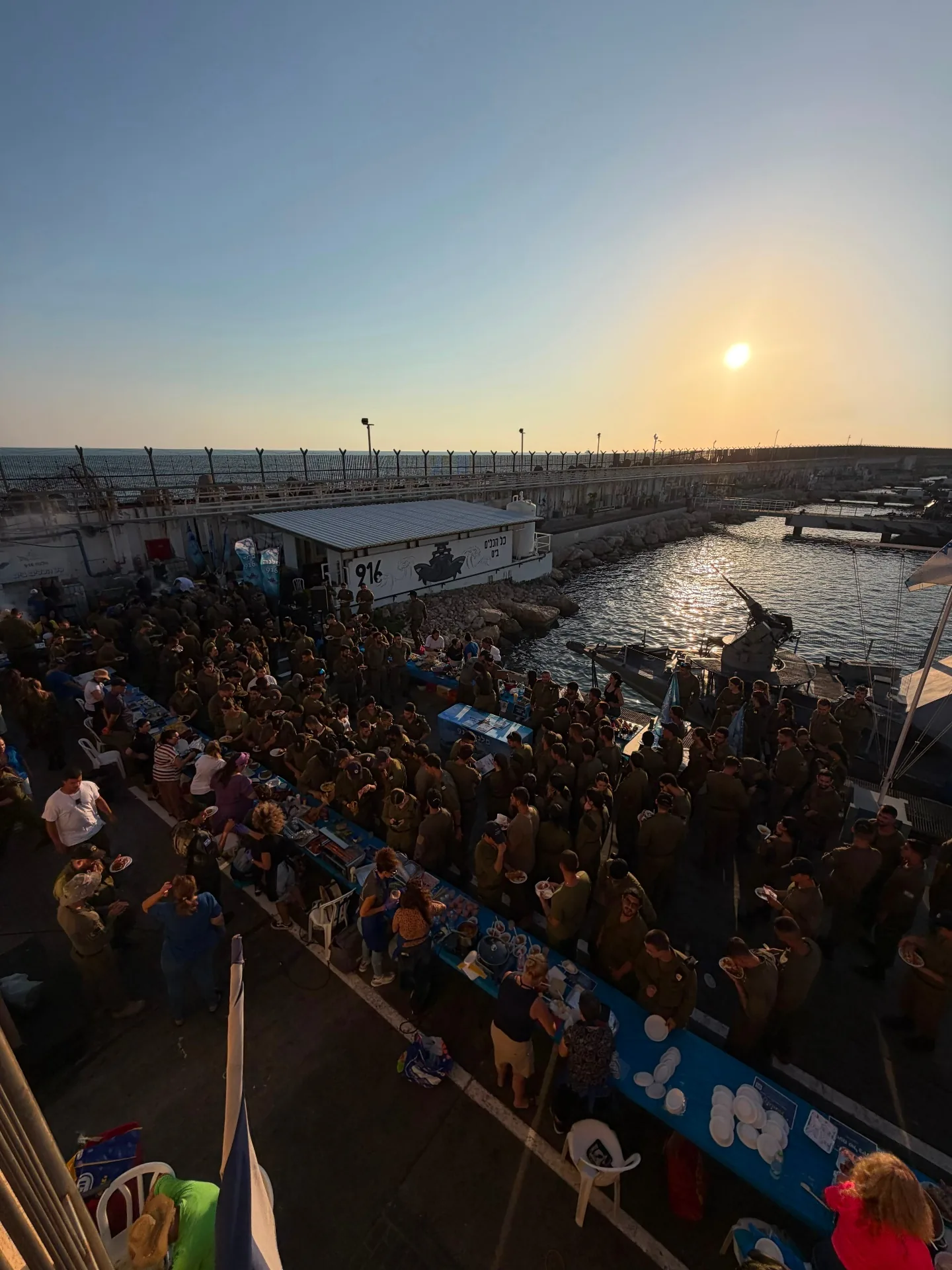 Golden-hour overview of the 916 flotilla evening of appreciation, with soldiers gathered around long tables at the harbor